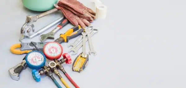 A collection of tools including wrenches, pliers, a utility knife, gauges, gloves, and a pipe cutter arranged on a light surface.