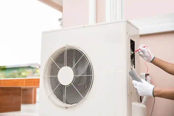Person wearing gloves is inspecting an outdoor air conditioning unit with a multimeter.